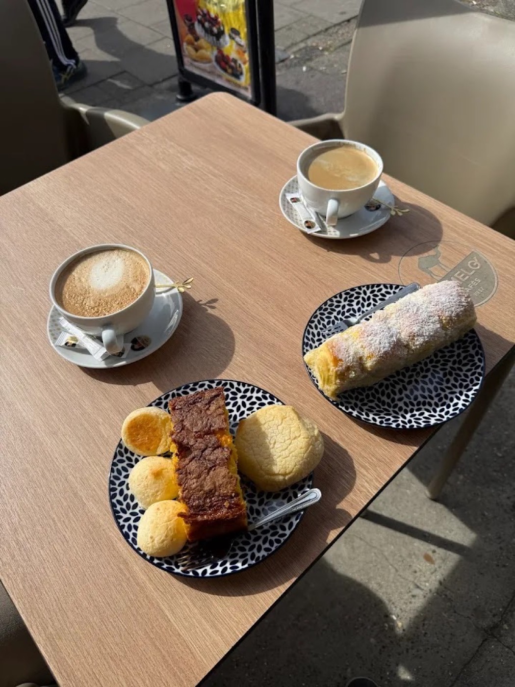 Two coffees and a plate of bakes on a sunny pavement table